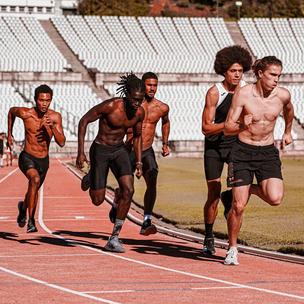 A sprinter mid-stride on a clay track at golden hour, motion blur on the limbs with sweat catching the sun.